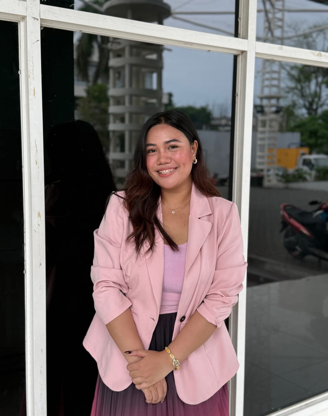 Aliyha in a pink blazer and pleated skirt, standing outside a building