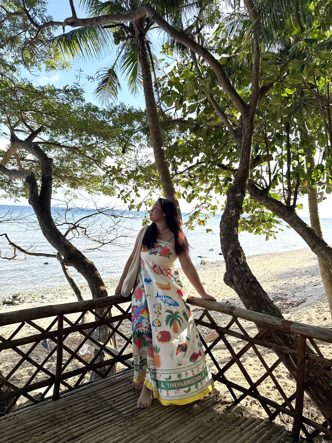 Aliyha standing on a bamboo deck beneath tree branches, looking out to the sea